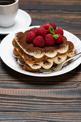 portion of Classic tiramisu dessert with raspberries and cup of espresso coffee isolated on wooden background