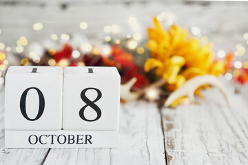 White wood calendar blocks with the date October 8th and autumn decorations over a wooden table. Selective focus with blurred background.