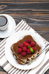 portion of Classic tiramisu dessert with raspberries and cup of espresso coffee isolated on wooden background
