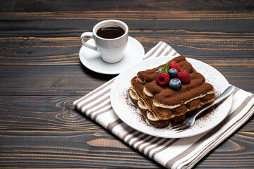 portion of Classic tiramisu dessert with raspberries. blueberries and cup of espresso coffee isolated on wooden background