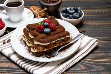 portion of Classic tiramisu dessert with raspberries. blueberries and cup of espresso coffee isolated on wooden background