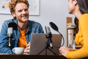 selective focus of excited redhead radio host interviewing young woman in studio