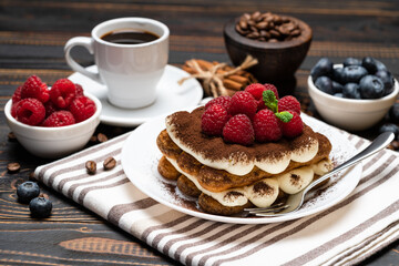 portion of Classic tiramisu dessert with raspberries. blueberries and cup of espresso coffee isolated on wooden background