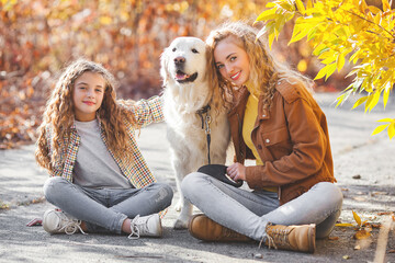 Two cute girls walking with their pet. Sisters and dog at autumn background