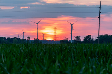 Wind turbines / wind mills/ wind power with high power wires / lines partially silhouetted by a sun...