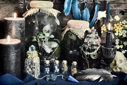 Styled still life with magic bottles with potions and herbs, runes, black candles and skull on witch table. Esoteric, gothic and occult background, Halloween mystic concept.