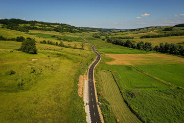 Naklejka premium Drone photograph with new asphalt road crossing a beautiful hilly landscape in summer season