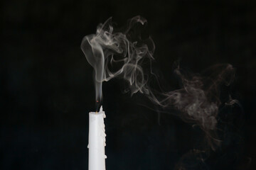 An extinguished candle with smoke and a red wisp on the wick.
