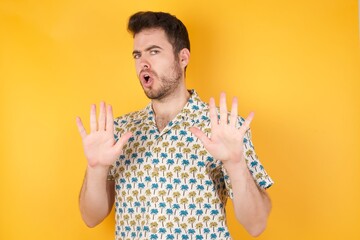 Young man wearing hawaiian shirt over yellow isolated background Moving away hands palms showing...