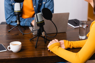 cropped view of interviewer and guest near microphones and laptop in radio studio