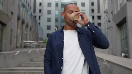Handsome young businessman drinking coffee using smartphone. Tracking shot of ethnic adult man sipping hot drink to go and browsing smartphone while walking on steps on city street