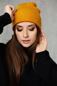 Close portrait of a hipster model girl with gentle makeup in a yellow hat and black sweatshirt.