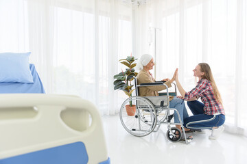 The senior breast cancer patient sitting on a wheelchair and her daughter touching hand together in the hospital room, cancer concept