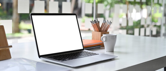 Mockup image of blank screen laptop computer and a cup of coffee with other office supplies at office.