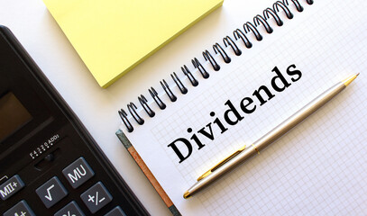 Notepad with text DIVIDENDS, next to it lies a calculator and yellow note papers. Business concept.