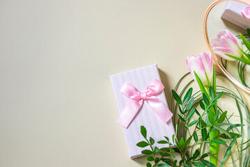 Gift box and pink tulip on a beige background. The concept of festive events and gift wrapping. Festive background.