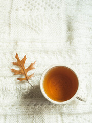 Autumn composition. Frame made of knitted plaid or scarf, cup of tea and fallen leave. Autumn, fall concept. Flat lay, top view, copy space.