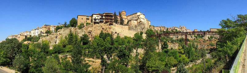 Obraz premium Old town of Cuenca, Spain, seen from the other side of the canyon (hoz) of the Huécar river. Central the famous hanging houses (cases colgadas). To the right the iron San Pedro pedstrian bridge. 