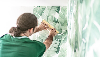 Tapezierer drückt die frisch verklebte Tapete mit dem Tapezierwischer an die Wand 