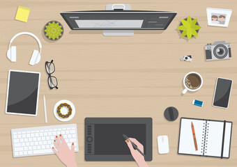 Wood textured table from top view with hands of woman drawing on digital graphic tablet with monitor, camera, tablet, headphones and gadgets, design for work from home concept