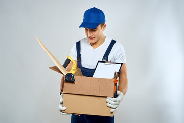man in working uniform with a box in his hands tools loader delivery light background