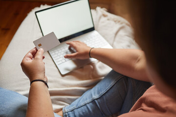Close-up of woman paying online by credit card using her laptop on the bed in the bedroom