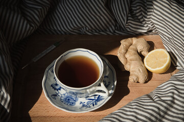 Ginger tea on the wooden plate in the bed. thermometer, self care for the flu, typical autumn still life