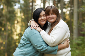 Portrait of two young lesbians embracing each other and smiling at camera while standing in the...