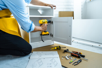 Man doing renovation work at home drilling wood with drill tack on locker