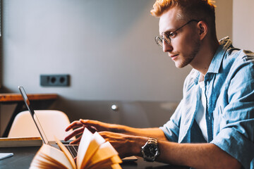 Focused caucasian man college student in glasses studying with books laptop distantly preparing for test exam writing essay doing homework at home, distantly education concept.