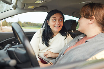 Young smiling woman talking to her girlfriend while she driving the car