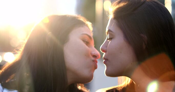 Two lesbian girlfriends kissing outside with sunflare. Beautiful moment between two LGBT lovers