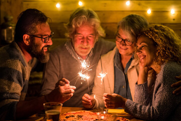 group of people celebrating the 2021 new year after a hard 2020 - bye 2020 concept - family enjoying and having fun together with sparklers at home eating pizza at dinner - christimas concept