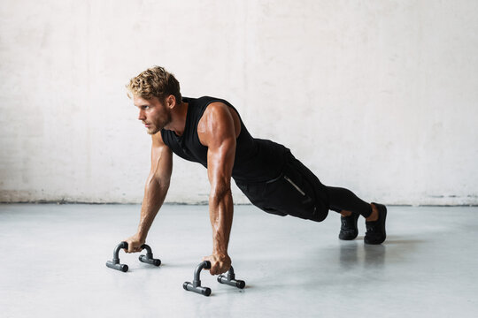 Photo of athletic young sportsman working out with push-up stops