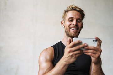 Photo of athletic joyful sportsman in earphones using mobile phone
