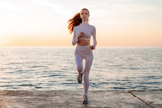 Image of redhead sportswoman running while working out on promenade