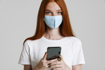 Photo of ginger beautiful girl in face mask using mobile phone