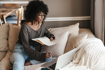 Image of woman working with laptop and papers while sitting on sofa