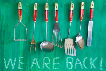 restaurant kitchen utensils on green painted wall, with message we are back. Restart gastronomy...
