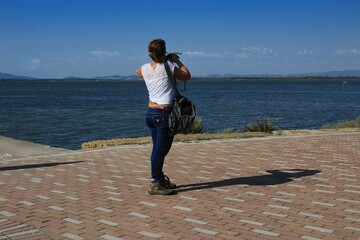 Young Woman Exploring the Coast of Orbetello, Tuscany - sportswear and binoculars -  sea view to admire - geometric pavement of the seafront