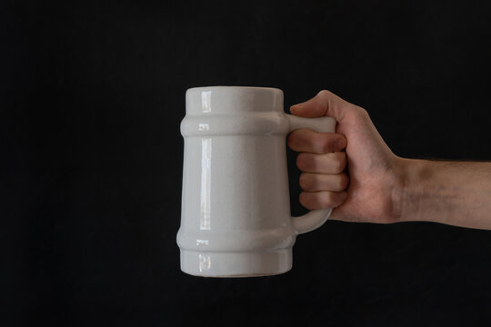 Man's hand holding a white ceramic beer mug. Isolated with black background.
