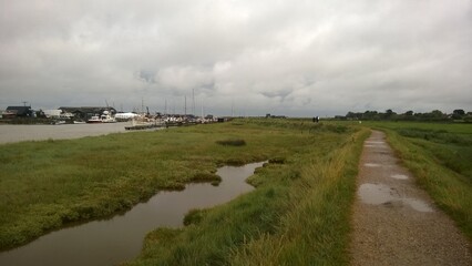 Landscape view of muddy walk along river Blyth estuary ferry between Southwold Walberswick Suffolk harbour by  beach with mooring boats on stormy evening grey cloud sky on late Summer holiday
