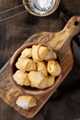 Lots of bagels. Puff pastry in a wooden plate on a brown table. Cookies close-up. Top view