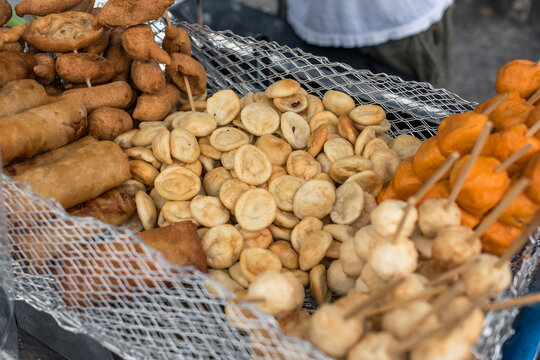 A foodstall in Manila offering freid Lumpia, Kikiam, Fishballs, Kwek Kwek and Squidballs placed in a grate.