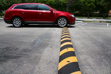 Red Minivan Driving Up to and Just Connecting with Yellow and Black Striped Speed Bump in Parking...