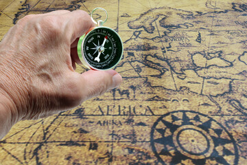 Classic round compass in hand on background of old vintage map of world as symbol of tourism with compass, travel with compass and outdoor activities with compass