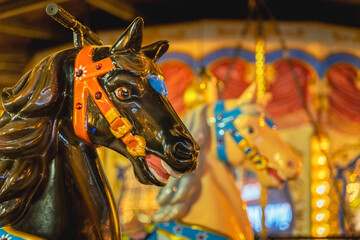 Portrait of painted dark wooden horse on fairground carousel, city attraction, selective focus