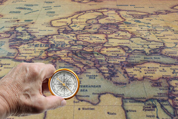 Classic round compass in hand on background of old vintage map of world as symbol of tourism with compass, travel with compass and outdoor activities with compass