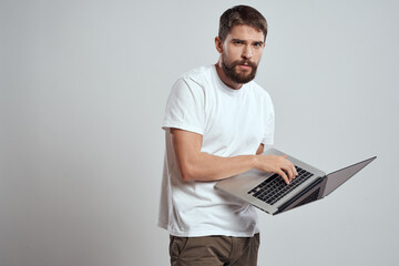 A man with a laptop in his hands on a light background in a white t-shirt emotions light background new technologies