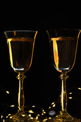 Christmas background concept. Two glasses with champagne and garland lights on a black background.